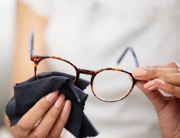 Photo of Cropped shot of an unrecognizable woman standing alone and using a cloth to clean her glasses