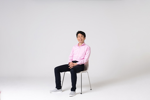 Full-length portrait of an Asian man on a white background.\nFull body shot. Japanese male, 30s.\nHealthy and confident figure.\nsitting on a chair. smiling.