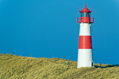 Red and white striped lighthouse on sand dunes of island Sylt, Germany
