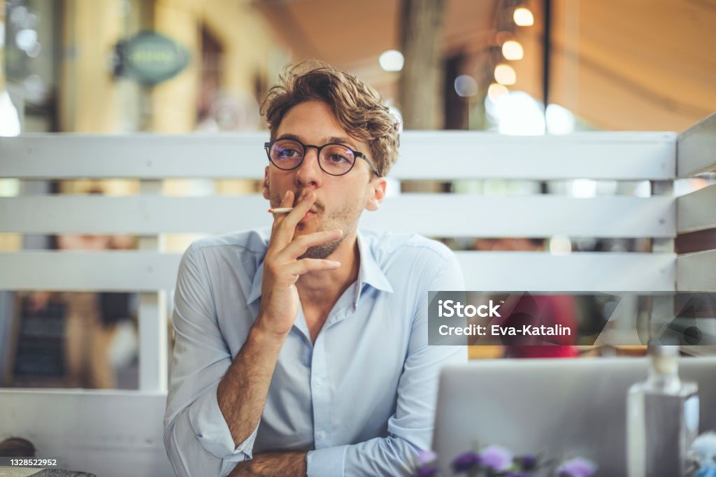 Young man smoking a cigarette in a sidewalk cafe Smoking - Activity Stock Photo