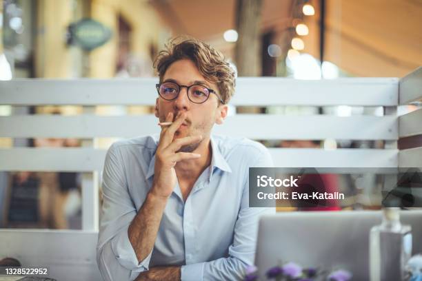 Young Man Smoking A Cigarette In A Sidewalk Cafe Stock Photo - Download Image Now - Smoking - Activity, Young Men, Cigarette
