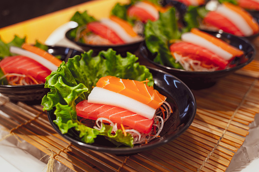 A woman hand wields chopsticks to delicately place fresh salmon sashimi on a plate in a Japanese restaurant, capturing the art of dining.