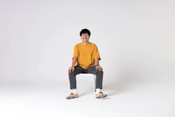 Full-length portrait of an Asian man on a white background.
Full body shot. Japanese male, 30s.
Healthy and confident figure.
sitting on a chair. smiling.
Looking at camera.
Shot in a studio with a white background.
Horizontal shot.