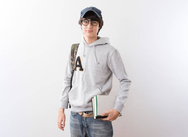 Handsome teen boy students wearing hoodie and glasses carrying a backpack and books standing on white background.