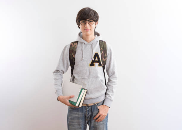 istock Handsome teen boy students carrying a backpack and books standing on white background. 1328527948