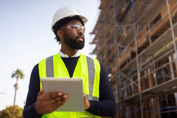 Young Black Male Project Manage with Safety Vest and Helmet A young black man is a project manager at a residential construction site. construction worker stock pictures, royalty-free photos & images