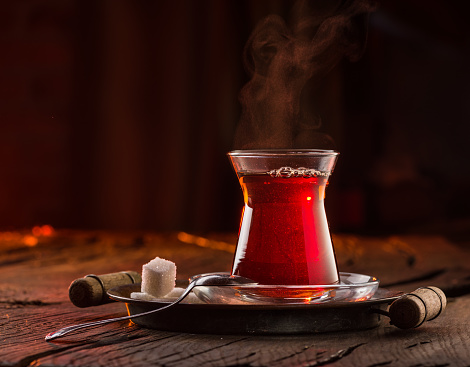 Glass with black traditional turkish tea stands on an old wooden table. Behind a dark background.