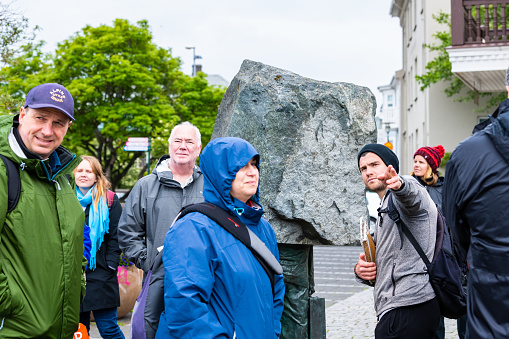 Reykjavik, Iceland - June 19, 2018: Candid group of people tourists on street with blue coats jackets on cold summer on sidewalk in downtown center rainy cloudy day