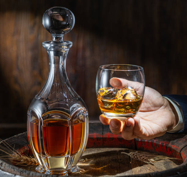 degustazione di whisky. l'uomo si siede davanti a una botte con un decanter e un bicchiere di whisky. - gin decanter whisky bottle foto e immagini stock