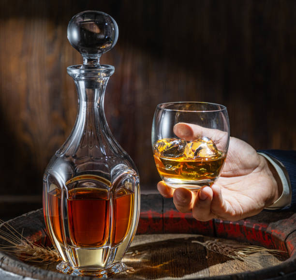 ウイスキーの試飲。男はデカンタとウイスキーのグラスで樽の前に座っています。 - whisky glass ice cube alcohol ストックフォトと画像