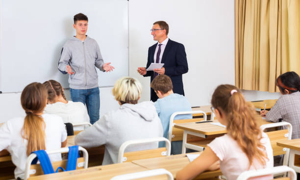 istock Positive schoolboy is standing near whiteboard and answer about task in classroom 1328530703