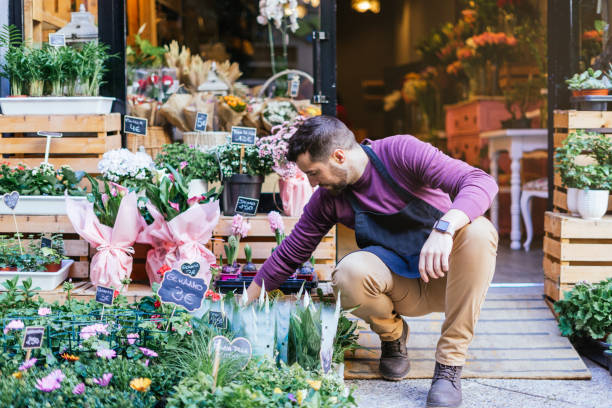 Flower store owner squatting down putting up the plants in the window. stock photo