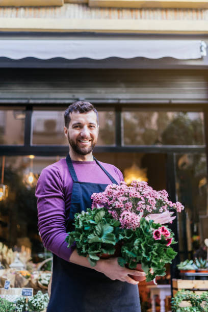 Young businessman showing a pot of plants in front of his store. Vertical photography. stock photo