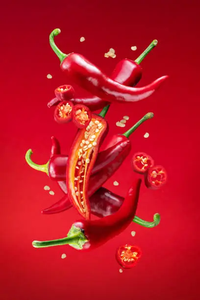 Photo of Fresh red chilli peppers and cross sections of chilli pepper with seeds floating in the air. File contains clipping paths.