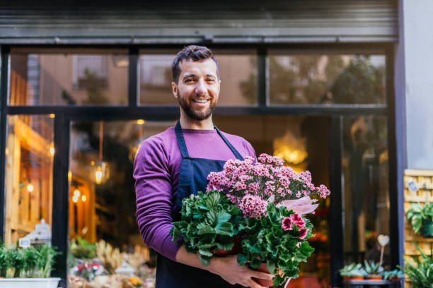 Young businessman showing a pot of plants in front of his store. Horizontal photography. stock photo