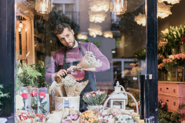 Florist sales clerk placing bouquets of flowers in his showcase through a glass window. stock photo
