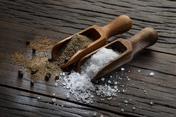 Photo of Sea salt and ground pepper in the wooden spoons on old wooden background. Two most popular ingredients that you put into food.