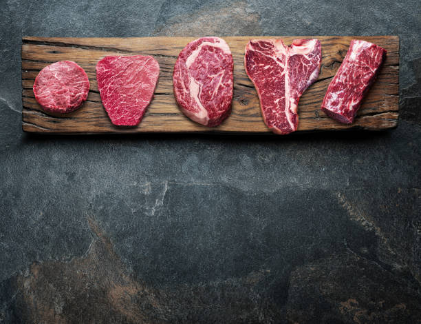 Different raw beef steaks on the wooden board on the grey table. Top view.