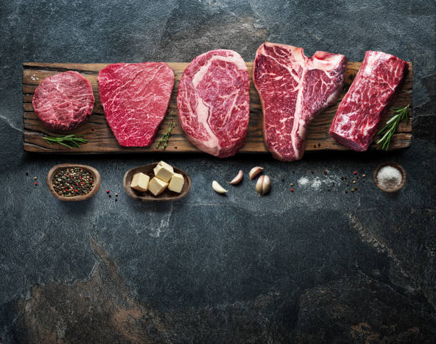 istock Different raw beef steaks on the wooden board on the grey table. Top view. 1328532182