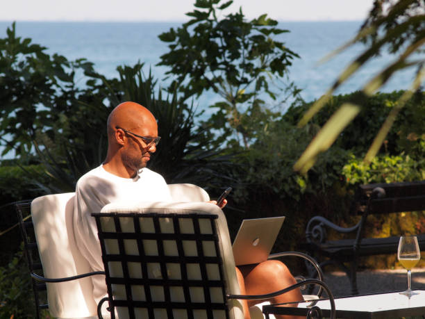 istock Man working  on vacation by the sea, using his laptop and smartphone 1328536080