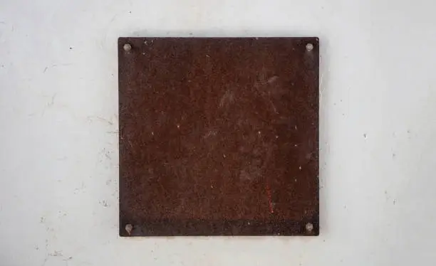 Photo of Empty sign plate, rusty metal brown color. mounted on white wall.