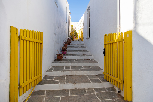 Greece. White house open yellow wood fence gate and traditional narrow stone stairs. Whitewashed walls and blue sky, summer sunny day at Sifnos island, Cyclades