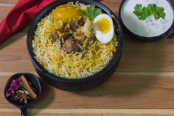delicious mutton biryani served in black pot with raita. kolkata style dum biryani with mutton, boiled egg and potato. wooden background.traditional mughlai delicacy. delicious mutton biryani served in black pot with raita. kolkata style dum biryani with mutton, boiled egg and potato. wooden background.traditional mughlai delicacy. kolkata stock pictures, royalty-free photos & images