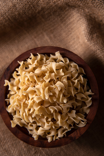 Raw Italian pasta in a bowl on brown background