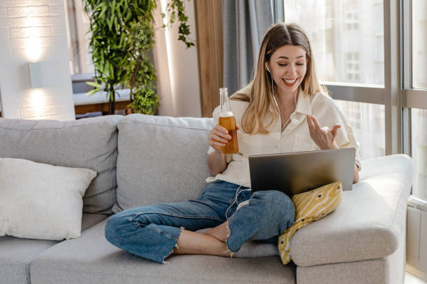 young woman is attending online party and drinking beer at home - after work beautiful people beer beer bottle imagens e fotografias de stock