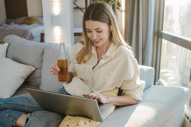 young woman is attending online party and drinking beer at home - after work beautiful people beer beer bottle imagens e fotografias de stock