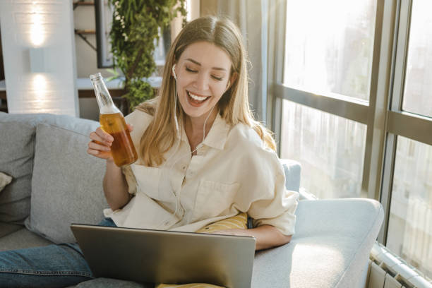 若い女性はオンラインパーティーに出席し、自宅でビールを飲んでいます - after work beautiful people beer beer bottle ストックフォトと画像