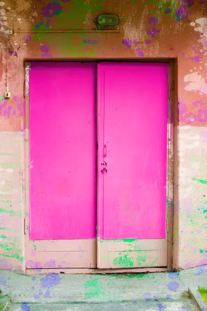 Photo of The old wooden doors are bright pink and the wall is covered with paint.