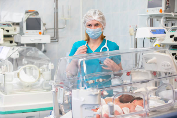 the children's doctor stands near the box with a newborn baby. - hospital nursery imagens e fotografias de stock