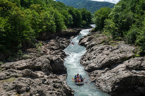 RUSSIA, ADYGEYA - July 14, 2019: Rafting in speedy mountain river with rock banks and forest on them. Active lifestyle, healthy and exciting adventure.