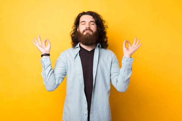 istock Bearded young man relaxes during meditation, keeps eyes closed, spreads palms sideways in nirvana over yellow background 1328552900