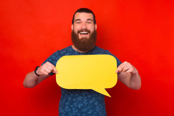 istock Happy smiling bearded man holding yellow bubble speech, looking at camera over red background 1328553089