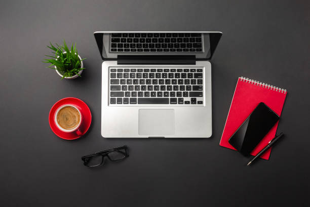 istock Black office desk table with blank screen laptop computer, notebook, mobile phone and red cup of coffee 1328555880