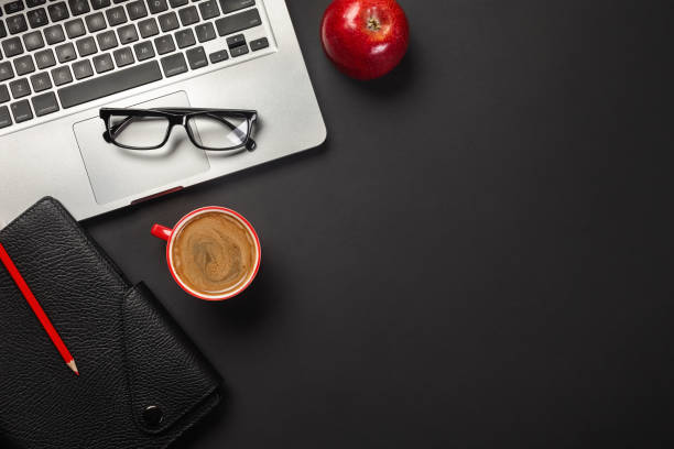 istock Black office desk table with blank screen laptop computer, notebook, cup of coffee, red apple and other office 1328555904