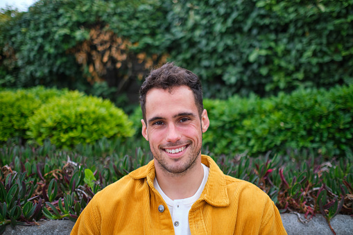 portrait of a smiling young man in a yellow shirt against a background of green bushes