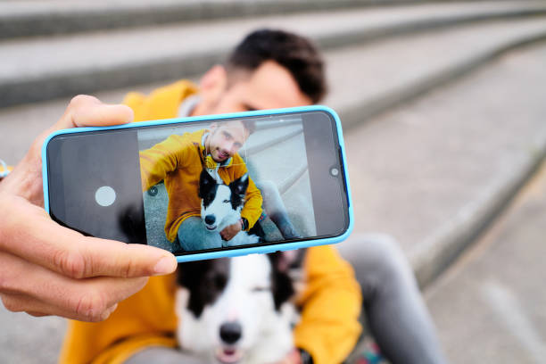 молодой человек фотографирует себя, обнимая собаку бордер-колли - color image pets well dressed dog стоковые фото и изображения