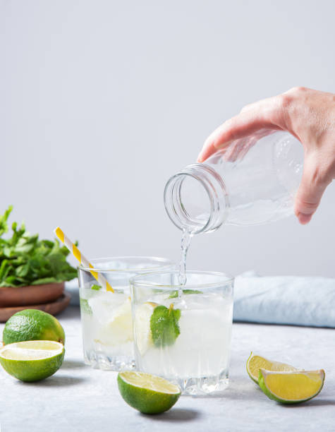 istock a hand pours a lime mojito lemonade into a glass on the table with lime slices and fresh mint. Front view and copy space 1328558992