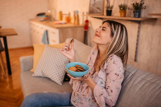 Beautiful woman eating cookies at home Portrait of beautiful emotional charming attractive sweet woman sitting on sofa in living room and eating cookies. home pampering stock pictures, royalty-free photos & images