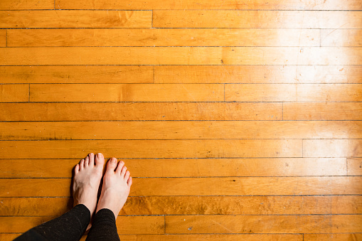 This is a wide angle photograph of a barefoot Caucasian woman’s feet standing on hardwood floors in Chicago, USA.