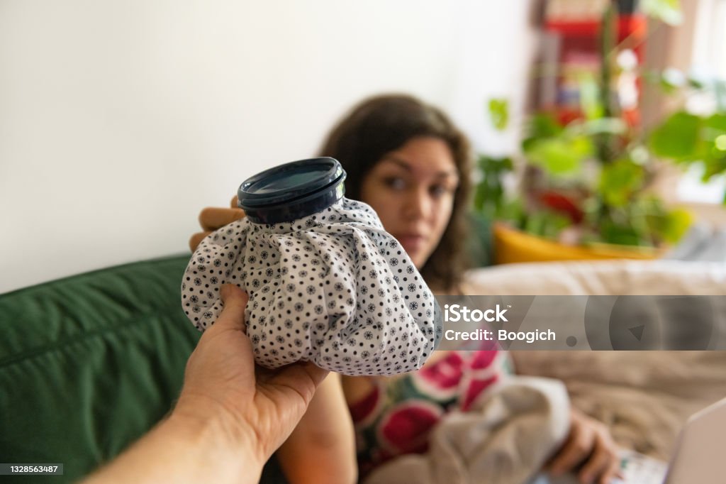 Ice Pack Being Handed to Injured Woman Resting at Home This is a photograph of an ice pack being handed to a young injured Hispanic woman resting at home. Ice Pack Stock Photo