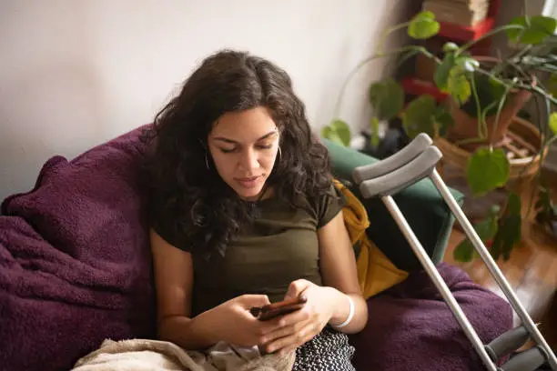 This is a photograph from a high angle view of an injured millennial Puerto Rican woman texting while resting at home in Chicago, USA.