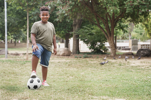 African American slightly overweight boy with soccer ball doing exercise in the park. slightly overweight little kid
