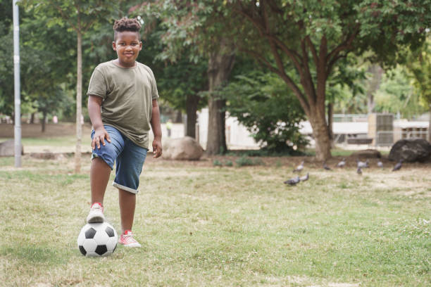 afro-americano um pouco acima do peso com bola de futebol fazendo exercício no parque. criança ligeiramente acima do peso - large build - fotografias e filmes do acervo