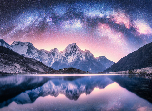 Milky Way over snowy mountains and lake at night. Landscape with snow covered high rocks, purple starry sky, reflection in water in Nepal. Sky with stars. Bright milky way in Himalayas. Space. Nature