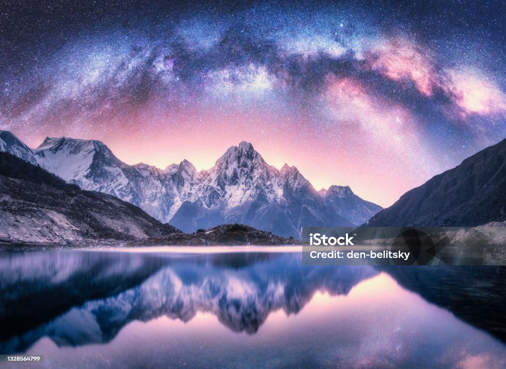 Milky Way over snowy mountains and lake at night. Landscape with snow covered high rocks, purple starry sky, reflection in water in Nepal. Sky with stars. Bright milky way in Himalayas. Space. Nature Mountain Stock Photo