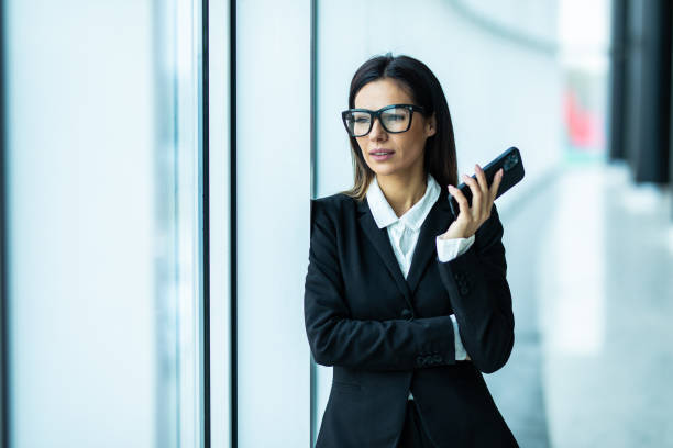 istock Female entrepreneur having conversation on mobile phone with business partner while standing near window of modern skyscraper 1328567184